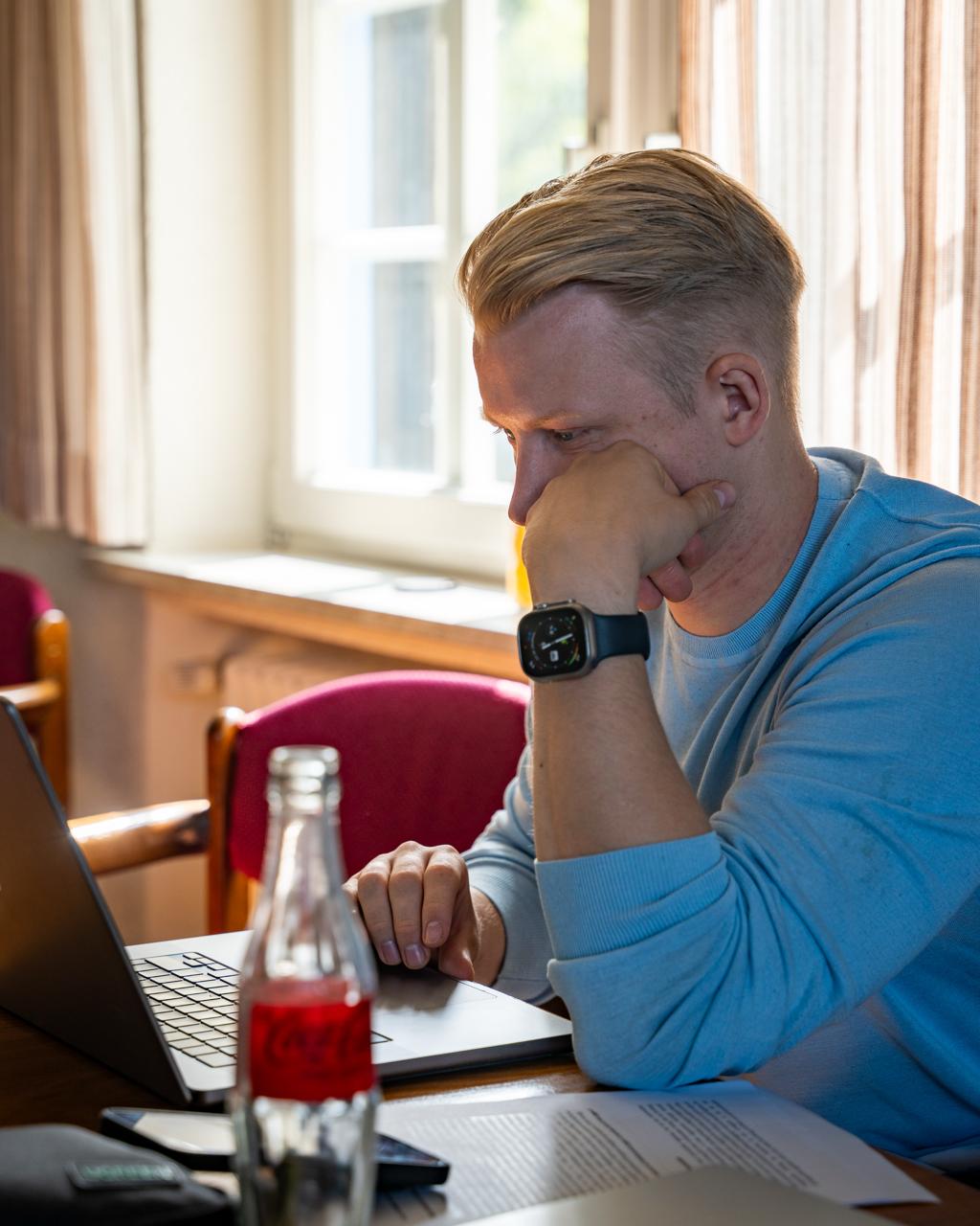 Finn Flebbe am Laptop über Studienunterlagen gebeugt